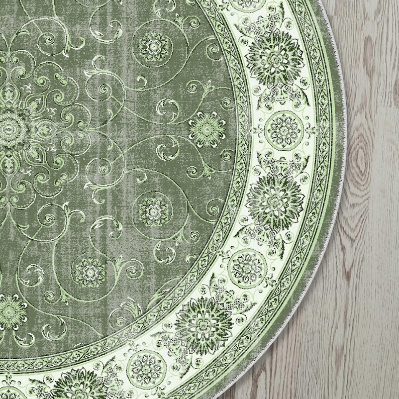 May include: A round, sage green rug with an ornate floral design. The rug features a central medallion and a decorative border with repeating floral patterns in shades of green and white. The rug's design includes swirling vines and floral motifs.