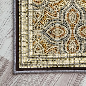 Può includere: Un tappeto in mosaico beige e marrone con un motivo geometrico. Il tappeto ha un bordo marrone scuro con un bordo beige chiaro.