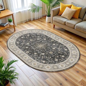 Pode incluir: Tapete oval com um centro cinza escuro com um padr&atilde;o floral em creme e bege. O tapete tem uma borda creme com medalh&otilde;es florais. O tapete &eacute; colocado em um piso de madeira.