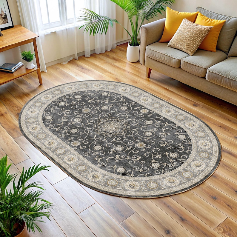 Pode incluir: Tapete oval com um centro cinza escuro com um padr&atilde;o floral em creme e bege. O tapete tem uma borda creme com medalh&otilde;es florais. O tapete &eacute; colocado em um piso de madeira.