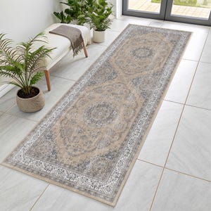 May include: A long rectangular runner rug featuring a beige background with intricate gray and white floral medallion patterns. The rug has a wide decorative border with detailed scrollwork and sits flat on a light-colored tiled floor surface.