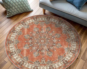 Puede incluir: Una alfombra redonda de color naranja y crema con un patrón floral. La alfombra tiene un aspecto desgastado y es perfecta para añadir un toque de estilo bohemio a cualquier habitación.