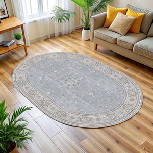Pode incluir: Um tapete oval com um centro azul claro e um padr&atilde;o floral detalhado. O tapete tem uma borda creme com um design repetitivo. &Eacute; colocado em um piso de madeira em uma sala de estar.