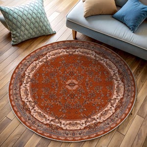 Pode incluir: Um tapete redondo de cor laranja e creme com um padrão floral. O tapete tem uma borda com um padrão repetitivo de folhas e flores.