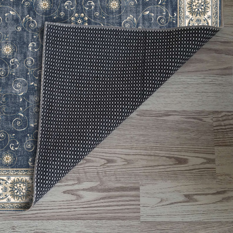 K&ouml;nnte beinhalten: Ein blauer und cremefarbener Teppich mit Muster und rutschfester R&uuml;ckseite. Der Teppich hat ein florales Design mit goldenen Akzenten.