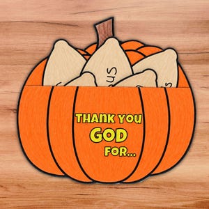 May include: A bright orange pumpkin-shaped cutout with a brown stem. The front features the yellow text "THANK YOU GOD FOR..." with a black outline. Several light-coloured, leaf-shaped wooden inserts are tucked into the top opening.