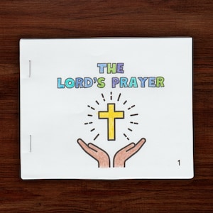 May include: A white booklet with the title "THE LORD'S PRAYER" in colorful letters. A yellow cross with a bright yellow halo is centered on the page. Two hands are reaching up towards the cross.