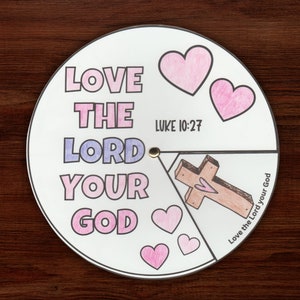 Puede incluir: Una rueda de papel imprimible, colorida, con las palabras "Ama al Señor tu Dios" y el versículo bíblico "Lucas 10:27". La rueda tiene una cruz con un corazón en el centro y corazones alrededor del borde.
