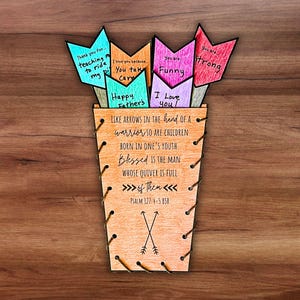 May include: A wooden Father's Day gift featuring a vase with colorful arrow-shaped cards. The cards have messages like "Thank you for teaching me to ride my bike" and "I love you because you take care." The vase has a Bible verse.