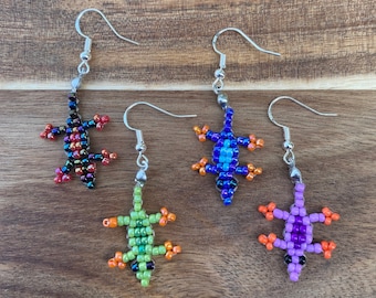 May include: Four pairs of beaded lizard earrings. Each pair features a different colour combination: red, orange, and black; blue, orange, and black; green, orange, and black; and purple, orange, and black.