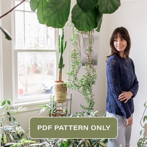 以下が含まれることがあります： 青いセーターを編むためのPDFパターン。セーターは、植物のある部屋でモデルに着用されています。