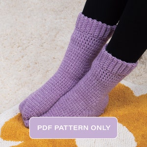 May include: A pair of lavender crochet socks with a textured stitch pattern. The socks are on a white and yellow rug. The text "PDF PATTERN ONLY" is on a lavender rectangle.