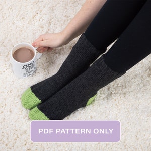 May include: A pair of black and green striped socks with a green cuff. The socks are worn by a person sitting on a white fluffy rug. The person is holding a white mug with the text "My soul is fed with the beauty of this world" printed on it.