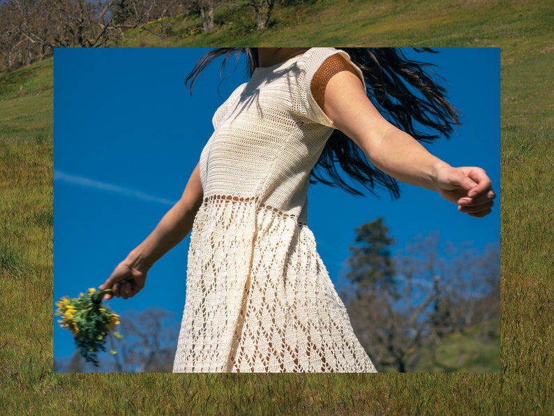 May include: A woman wearing a white crochet dress with a lacy pattern, standing in a field with a blue sky in the background.
