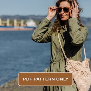 Pode incluir: Uma bolsa de crochê com detalhes de franjas, usada como bolsa transversal por uma pessoa que veste uma jaqueta verde e óculos de sol. A bolsa é de cor bege claro e tem uma textura tecida. O texto "PDF PATTERN ONLY" é visível na imagem.