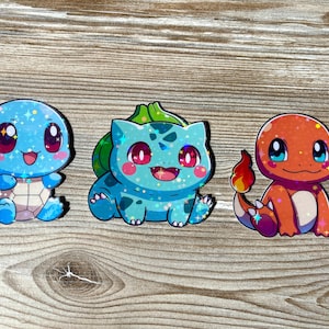 May include: Three cartoon character stickers with a sparkly, iridescent finish. The characters are Squirtle, Bulbasaur, and Charmander from the Pokemon franchise.