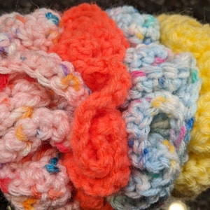 May include: A multi-colored crocheted headband with pink, orange, blue, and yellow yarn. The headband is made with a variety of stitches, including a ruffled edge.