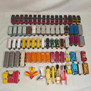 Könnte beinhalten: Eine Sammlung von Holzeisenbahnwagen in verschiedenen Farben und Designs, darunter Rot, Blau, Grün, Gelb und Schwarz. Die Wagen sind in Reihen angeordnet und umfassen sowohl Personen- als auch Güterwagen. Einige der Wagen haben Nummern aufgedruckt.