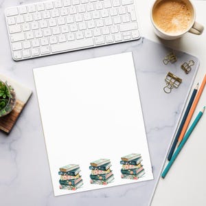May include: A white sheet of paper with three stacks of books illustrated at the bottom. The books have floral and patterned covers. A white keyboard, a cup of coffee, and pencils are on the desk.
