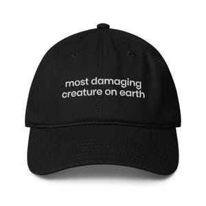 May include: Black baseball cap with white embroidered text reading "most damaging creature on earth". The cap features a curved peak and an adjustable strap.