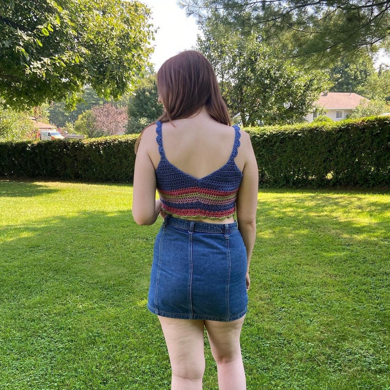 May include: A woman wearing a multi-colored crochet crop top with a denim skirt.