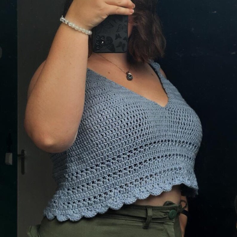 May include: A light blue crochet crop top with a scalloped hem. The top is sleeveless and has a V-neck.