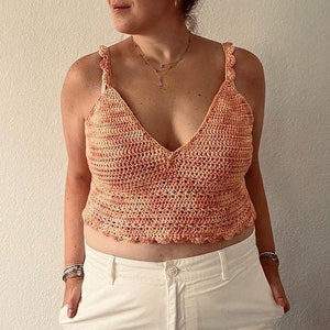 May include: A crocheted tank top with a V-neck and scalloped edges. The top is made in a peach and orange color scheme.