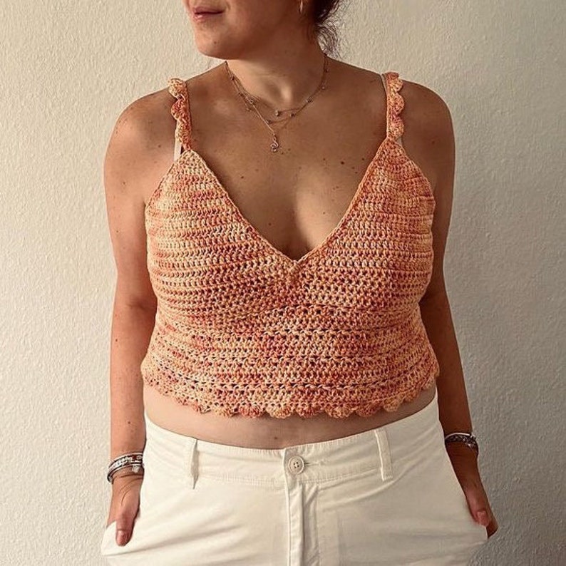 May include: A crocheted tank top with a V-neck and scalloped edges. The top is made in a peach and orange color scheme.