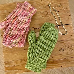 May include: A pair of knitted mittens, one pink and one green. The mittens are made with a textured stitch and have a simple, classic design.