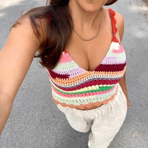 May include: A colorful crocheted crop top with a scalloped hem. The top features a variety of colors, including pink, red, orange, yellow, green, and blue.