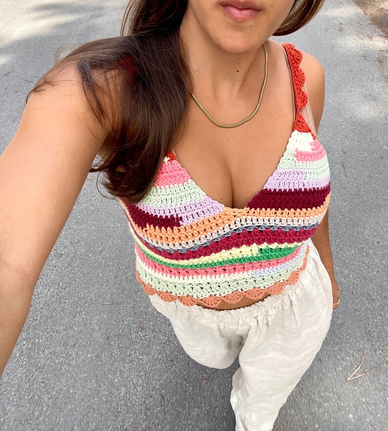 May include: A colorful crocheted crop top with a scalloped hem. The top features a variety of colors, including pink, red, orange, yellow, green, and blue.