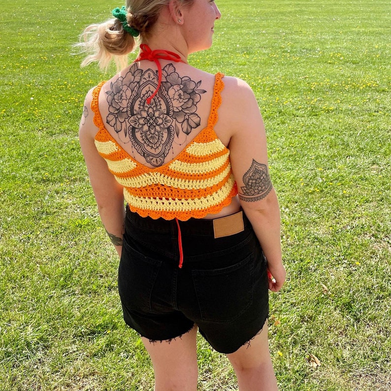 May include: A crocheted crop top with orange and yellow stripes and a scalloped hem. The top has a floral design on the back.