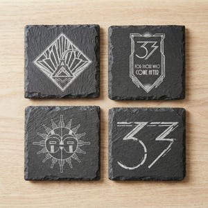 May include: Set of four square slate coasters with Art Deco-style designs. Each coaster features a unique white design, including geometric shapes, the number "33", and the text "FOR THOSE WHO COME AFTER".