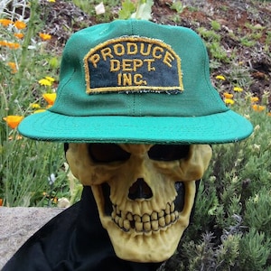 Puede incluir: Una gorra de béisbol verde con un parche negro y dorado que dice "PRODUCE DEPT. INC."