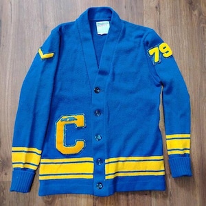 May include: A vintage blue cardigan sweater with yellow accents. Features a large yellow "C" patch, the number "79", and yellow stripes on the sleeves and hem. The sweater has a V-neck and button closure.