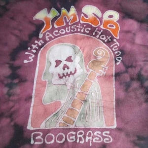 May include: A tie-dye t-shirt with a graphic of a skull playing a stringed instrument. The text reads "YMSB With Acoustic Hot Tuna" above the skull and "Boograss" below. The design is in shades of orange, white, and green.