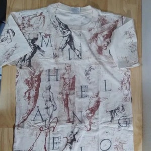 May include: A white t-shirt with a print of various sketches of human figures and the words "Michelangelo" in a vintage style.