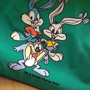 May include: A green fabric bag with a cartoon image of Bugs Bunny, Lola Bunny, and Taz. The image is in a vintage style and the text "TM & ©1995 Warner Bros" is printed at the bottom.