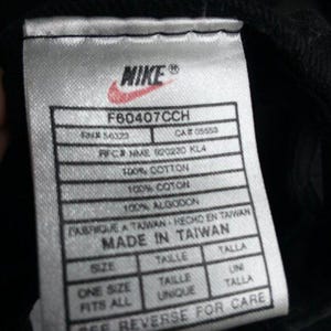May include: Close-up of a white tag with the Nike logo and text. The tag includes details such as "F60407CCH", "100% Cotton", and "Made in Taiwan". The tag also states "One Size Fits All".