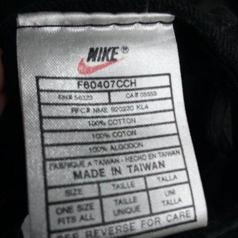 May include: Close-up of a white tag with the Nike logo and text. The tag includes details such as "F60407CCH", "100% Cotton", and "Made in Taiwan". The tag also states "One Size Fits All".