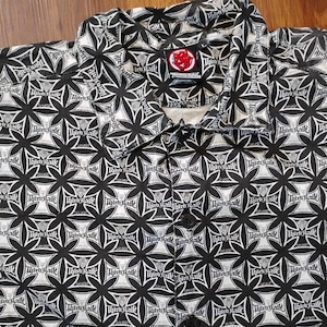 Puede incluir: Camisa abotonada en blanco y negro con un estampado floral repetido. La camisa tiene cuello y cierre de botones. El texto "Third Rail" es visible. La camisa está hecha de tela ligera.