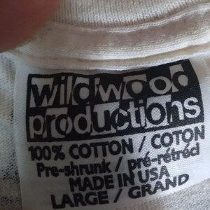May include: White tag with black text that reads "Wildwood Productions 100% Cotton/Coton Pre-shrunk/pr&eacute;-r&eacute;tr&eacute;ci MADE IN USA LARGE/GRAND"