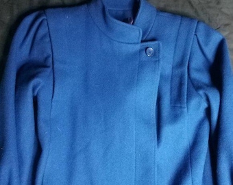 May include: A striking blue coat with a high collar and a single button fastening. The coat has a tailored silhouette with gentle shoulder shaping, presenting a classic and refined appearance. The material seems to be of a medium weight, ideal for cooler temperatures.