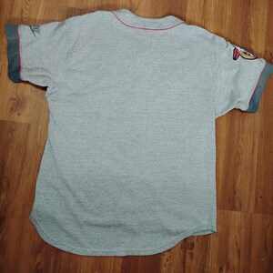 May include: A grey baseball jersey with a red neckline and dark green sleeve cuffs. The Nike logo is visible on the left sleeve. The jersey is laid out on a wooden surface.