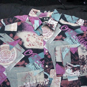 Puede incluir: Una camisa de botones con estampado negro, rosa, azul y blanco con cuello. La camisa tiene un bolsillo en el lado izquierdo y el texto "BTX" en la etiqueta.