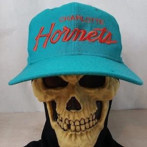 Może przedstawiać: Czapka bejsbolowa w kolorze turkusowym z haftowanym napisem "Charlotte Hornets" w kolorze czerwonym z przodu.