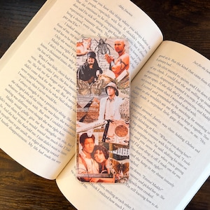 May include: A rectangular bookmark featuring a collage of images from a movie. The images include actors in various scenes, with a vintage aesthetic. The bookmark is placed between the pages of an open book, with text visible on the pages.