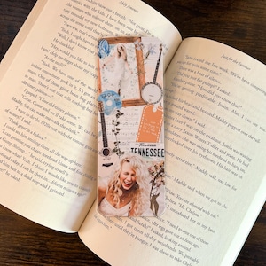 May include: A decorative bookmark featuring a collage of images, including a woman, a guitar, and a banjo. The bookmark has the word "Tennessee" on it. The bookmark is placed in an open book.