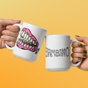 May include: Two white ceramic mugs. One mug has a pink and yellow cartoon image of a set of dentures with a winder key. The other mug has the word 'KAMBINO' written in black letters.