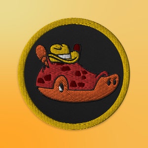 May include: A round, yellow-bordered patch with a black background features a cartoon illustration of a red and orange creature wearing a yellow cowboy hat. The creature has a spotted body and a wide smile.